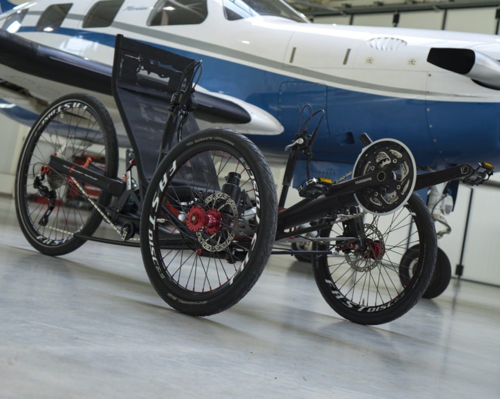 Full-suspension recumbent trike in front of airplane